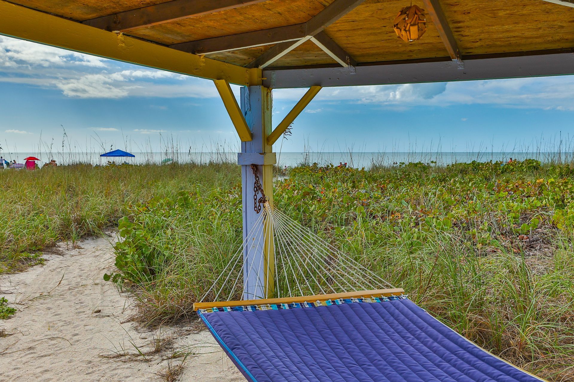 A purple gazebo is sitting on the beach next to a path leading to the ocean.