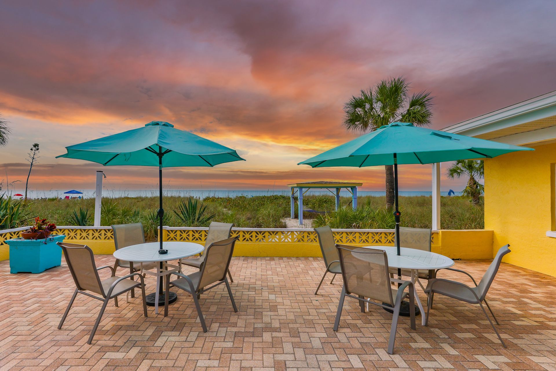 A patio with tables and chairs and umbrellas at sunset