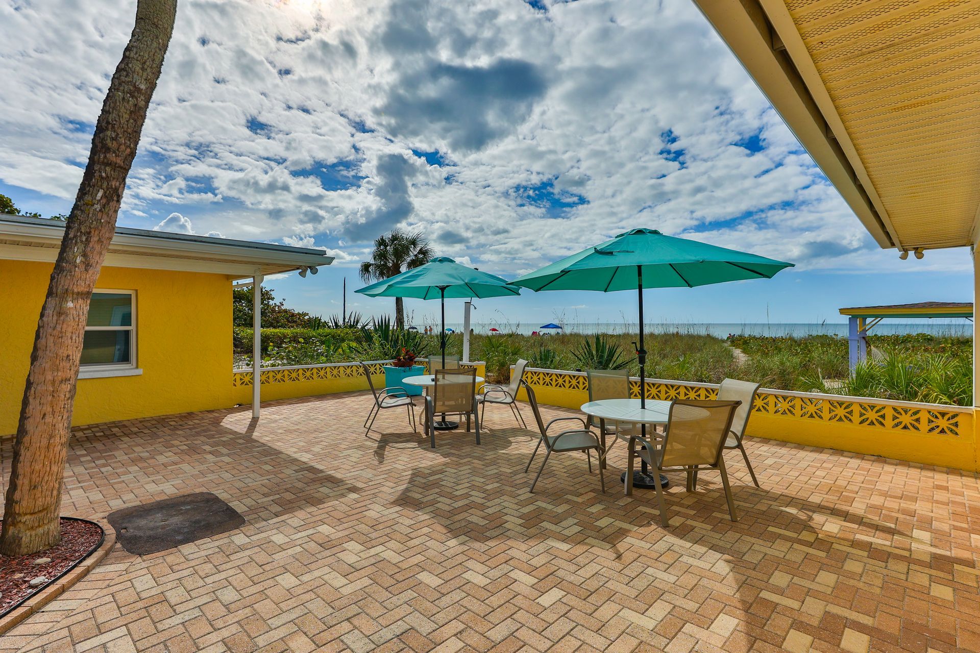 A yellow house with a patio with tables and chairs and umbrellas