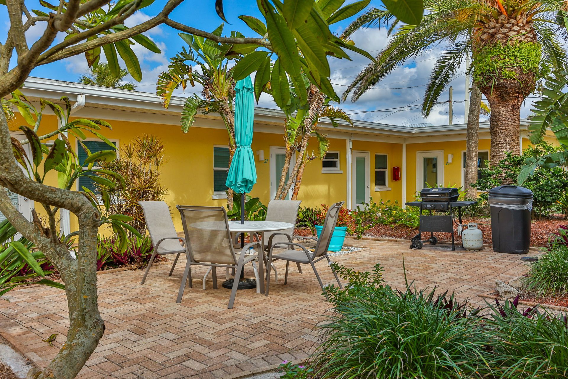 A patio with a table and chairs and an umbrella in front of a yellow house