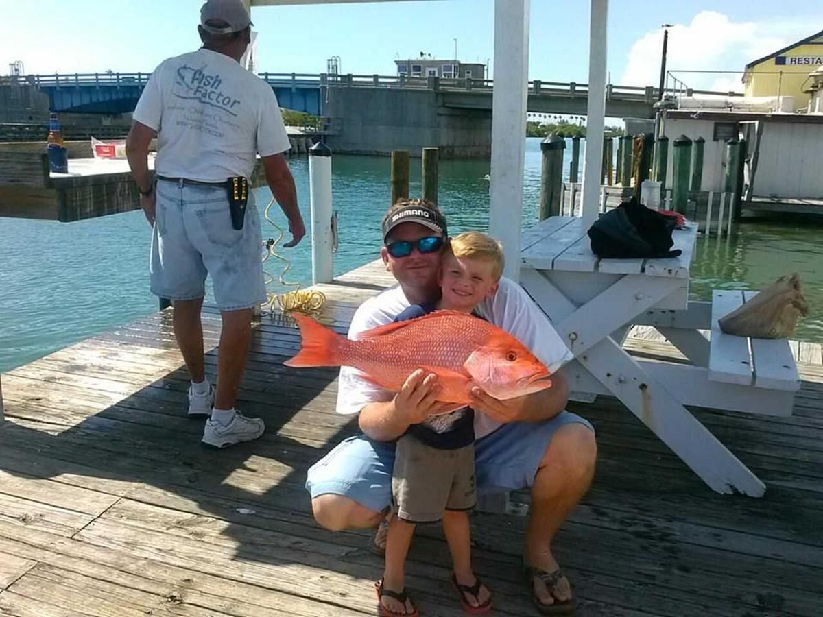 A man and child holding a large red fish on a dock
