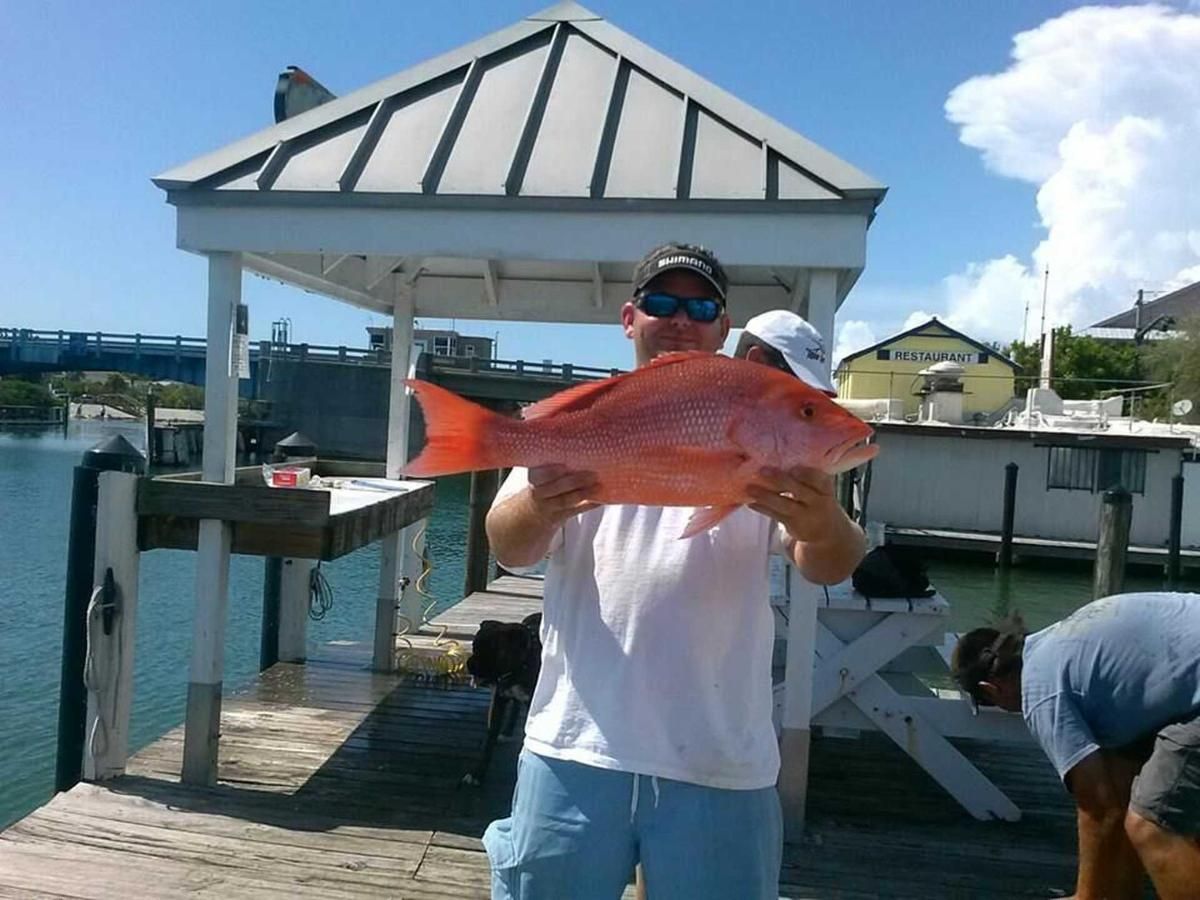 A man is holding a large red fish on a dock