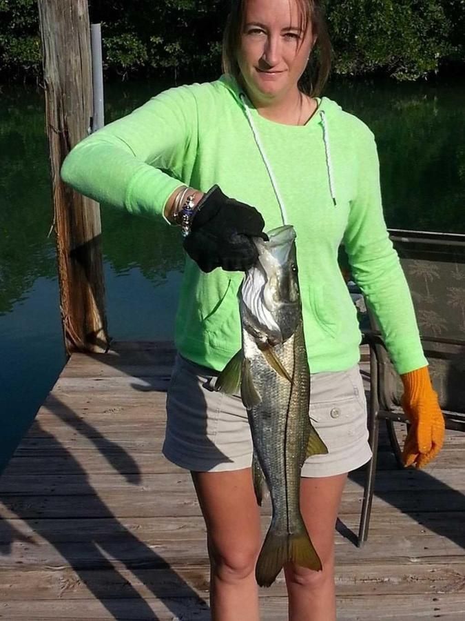 A woman in a green shirt is holding a large fish