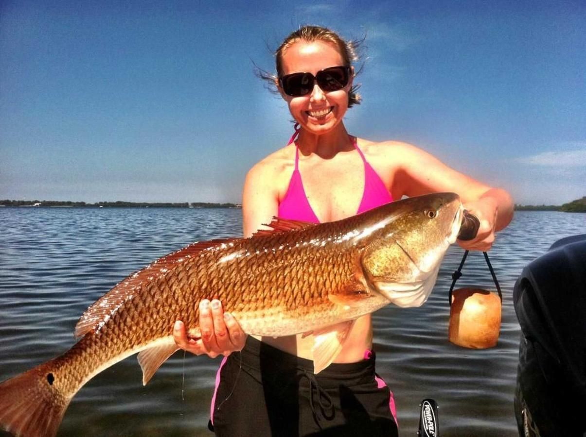A woman in a pink bikini is holding a large fish