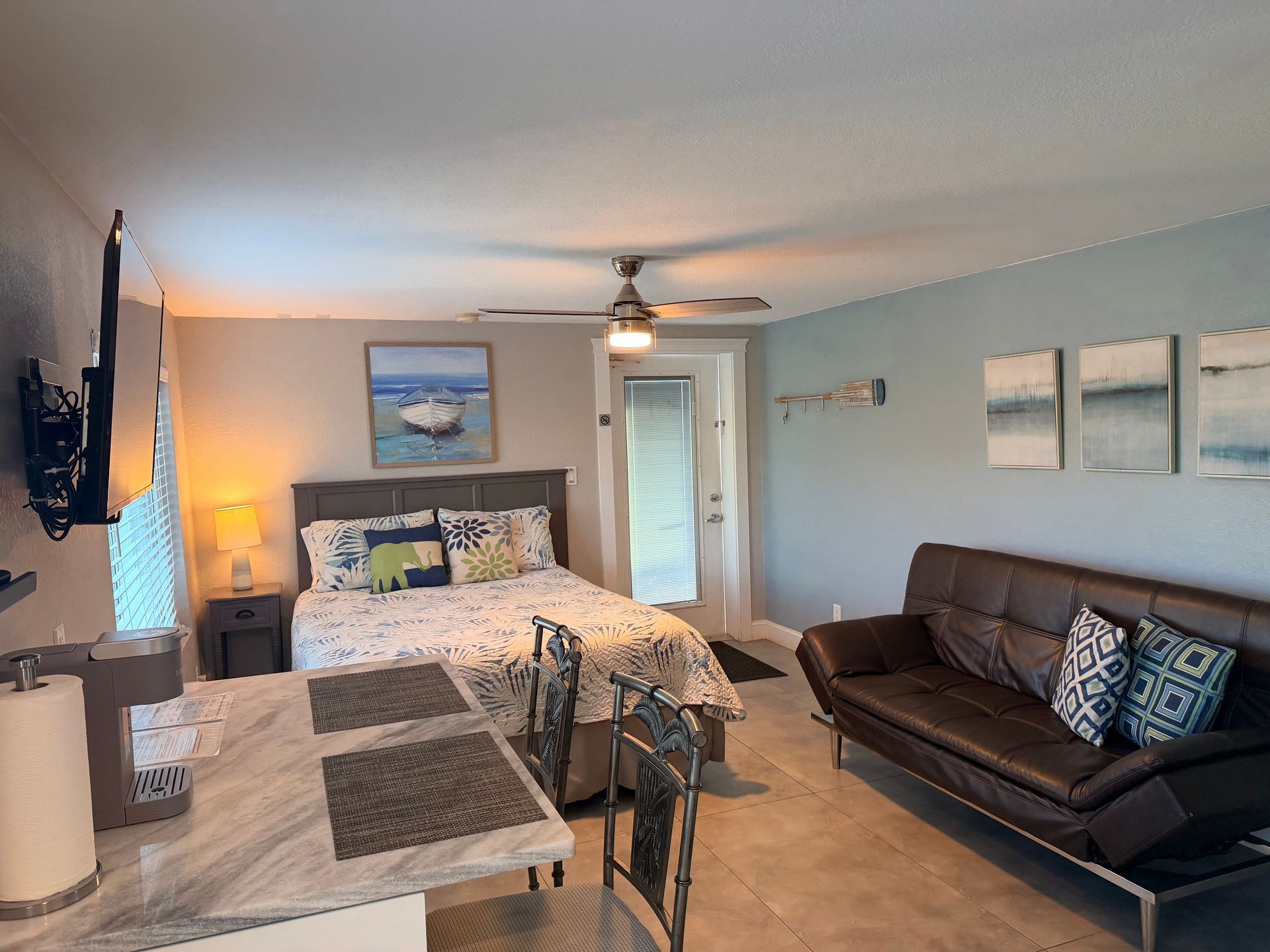 Small studio apartment with bed, sofa, kitchen counter, and wall art.