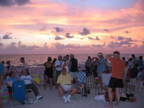 A group of people are gathered on the beach at sunset.