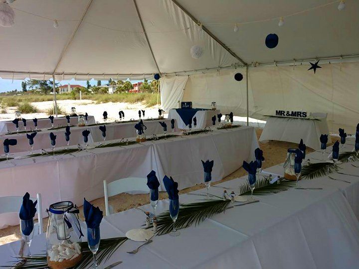 A long table with blue napkins and glasses under a tent