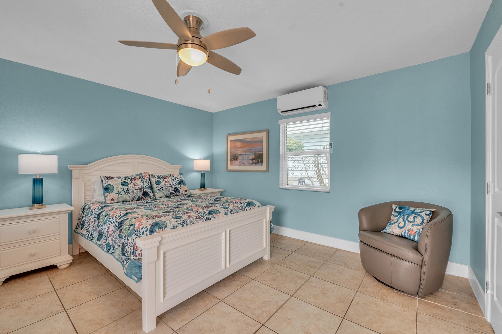A bedroom with a king size bed , chair , nightstand and ceiling fan.