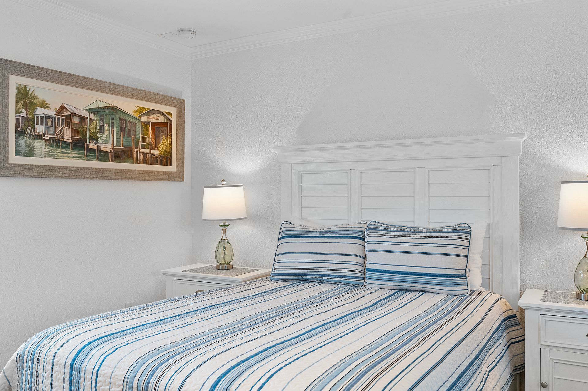 A bedroom with a bed , nightstand , lamps and a painting on the wall.