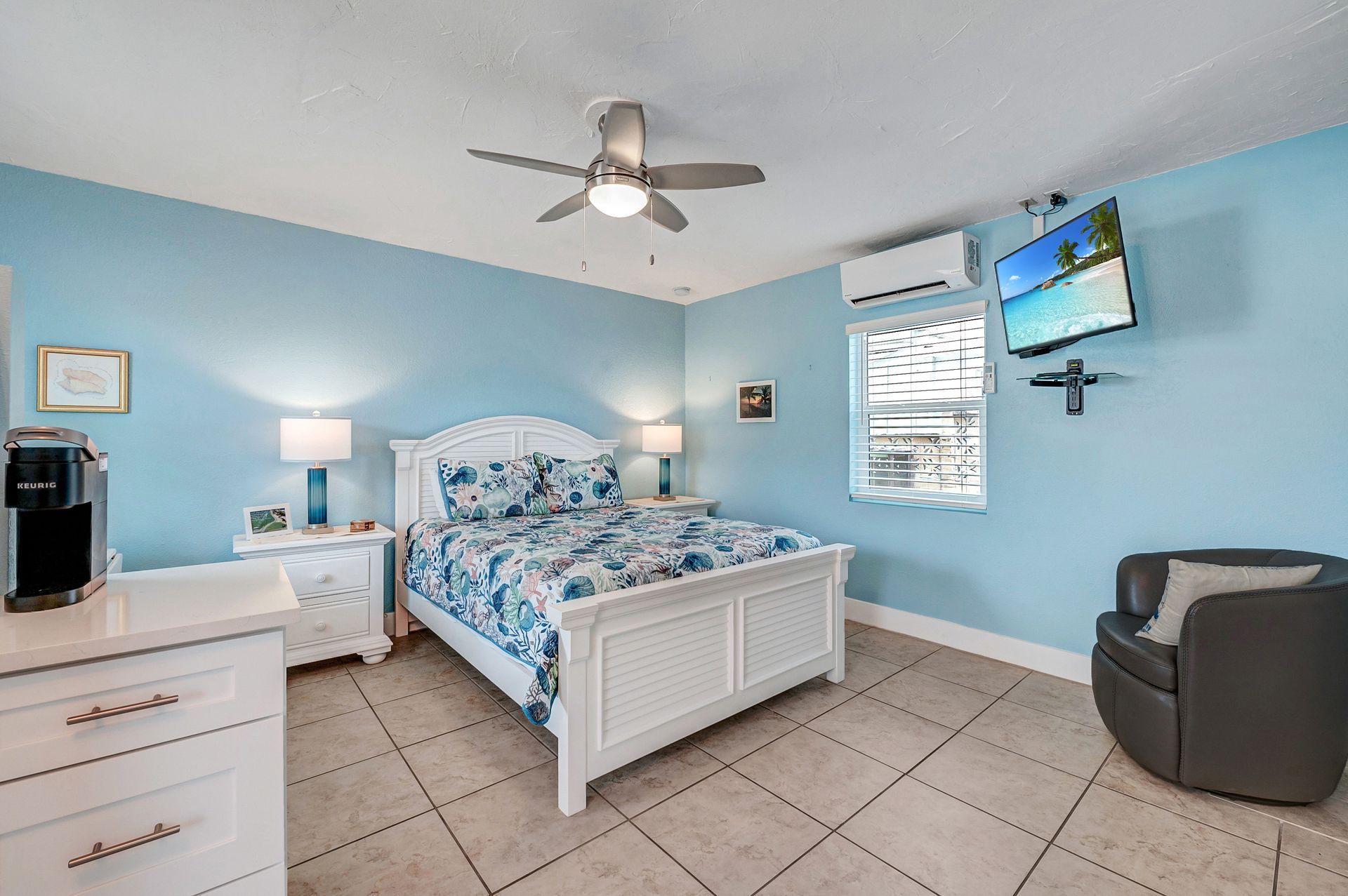 A bedroom with a bed , dresser , chair , television and ceiling fan.