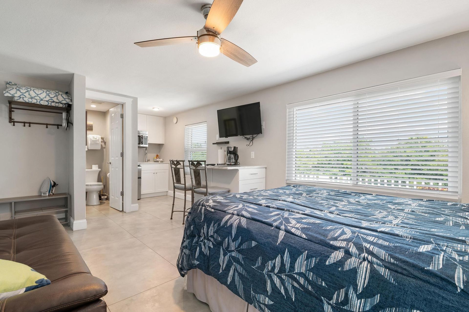 A bedroom with a king size bed, a ceiling fan, a flat screen tv and a couch.