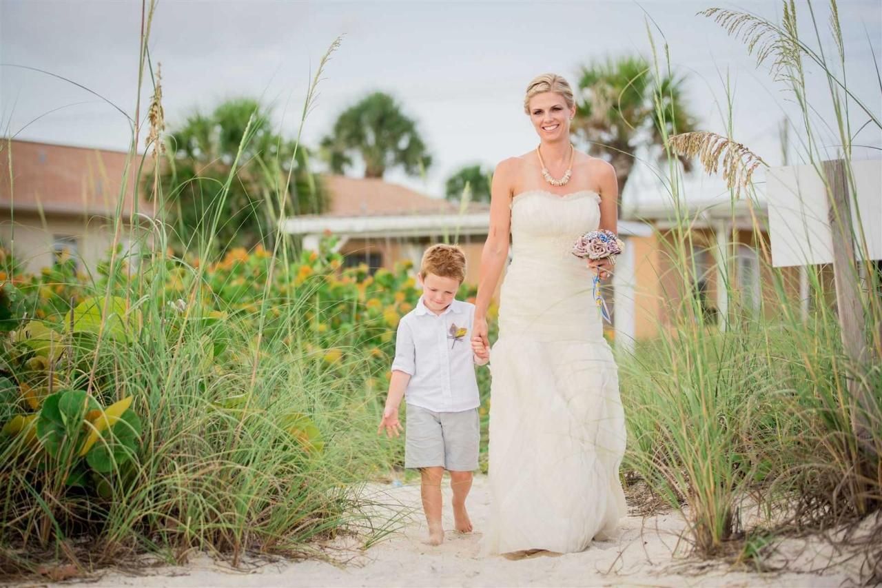 A bride and groom are walking down the beach holding hands.