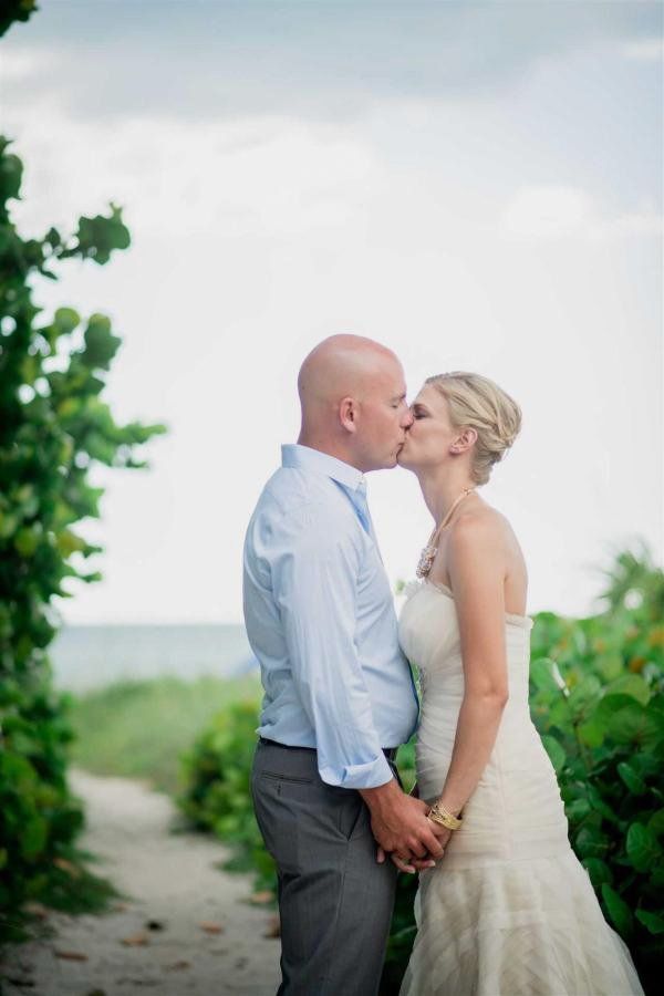 A bride and groom are kissing on a path next to the ocean.