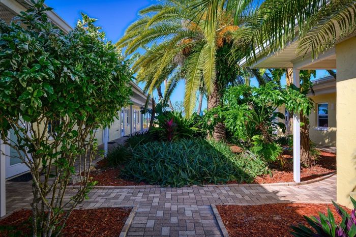 A brick walkway leading to a house with palm trees in the background.