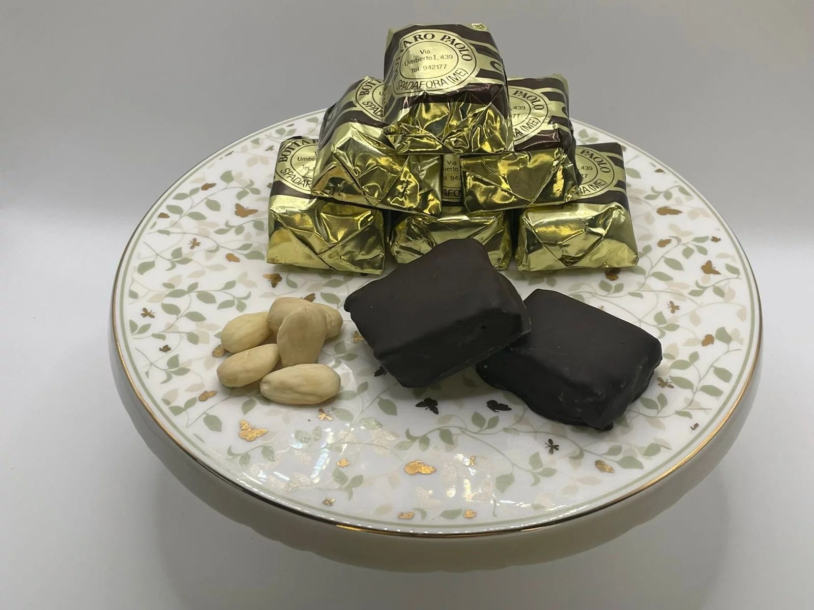 Cioccolatini avvolti in carta stagnola dorata su un piatto decorato con mandorle e un paio di pezzetti di cioccolato scartati.