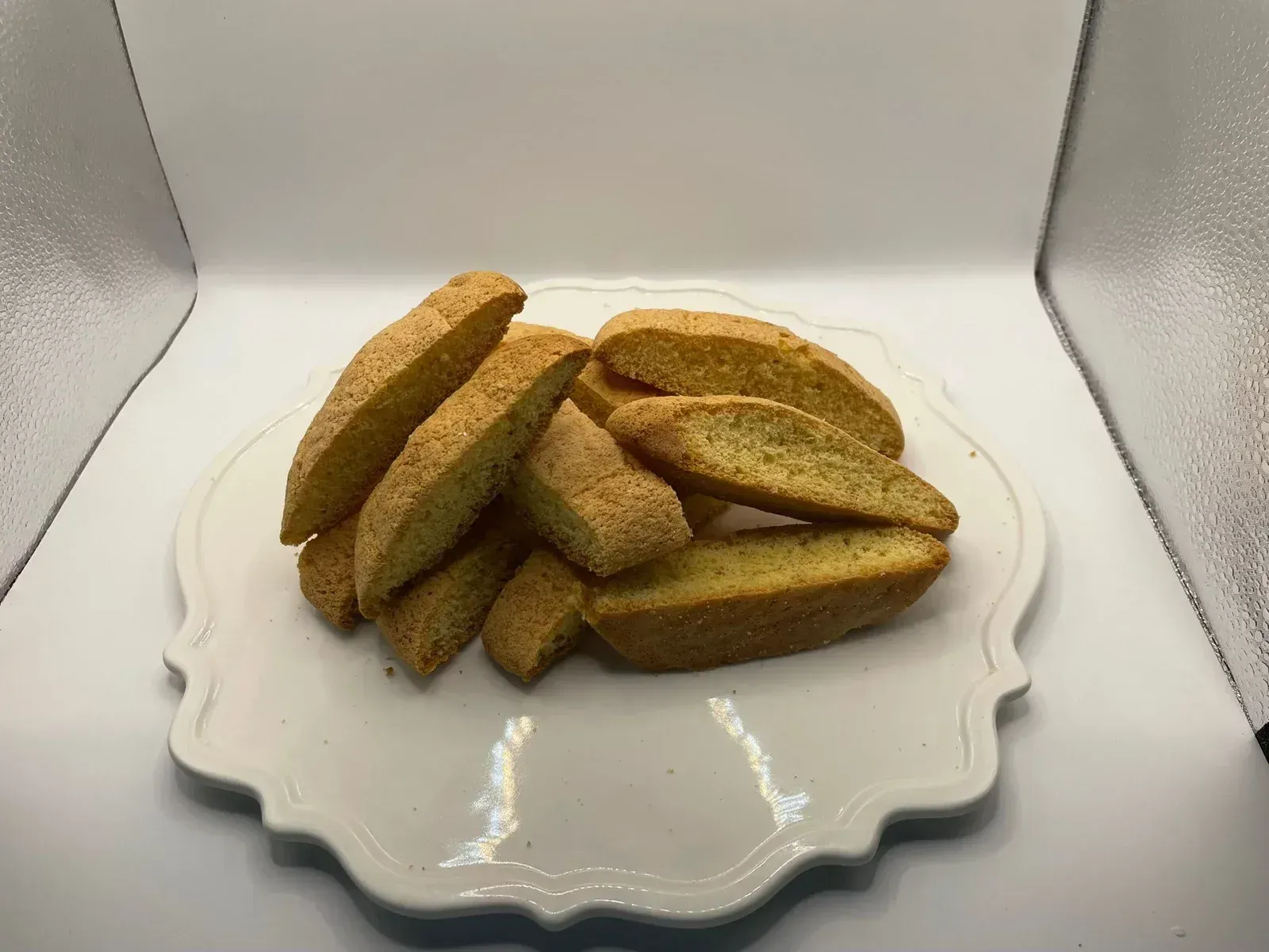Una pila di biscotti dorati su un piatto bianco con i bordi smerlati, su uno sfondo bianco brillante.
