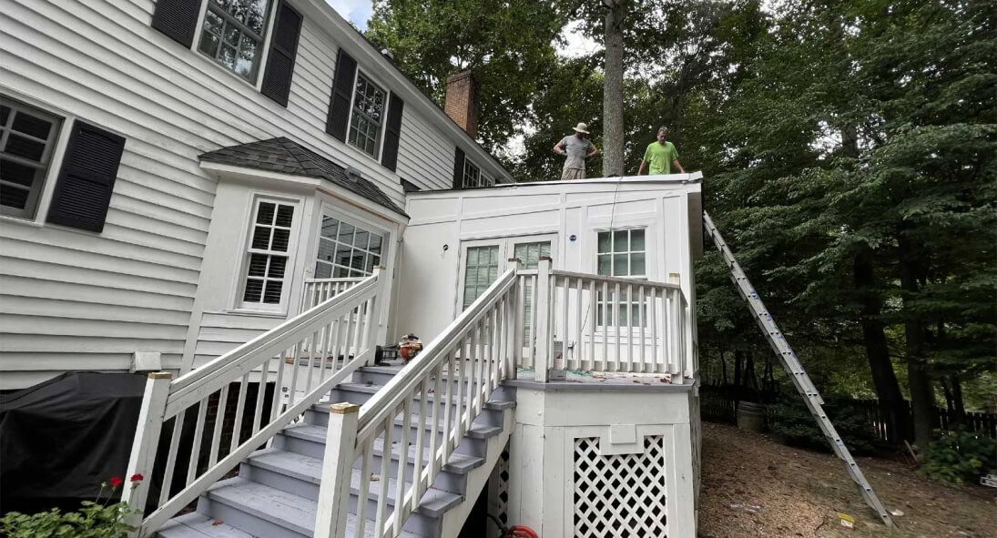 Roofing Services: A man is standing on top of a deck next to a house.