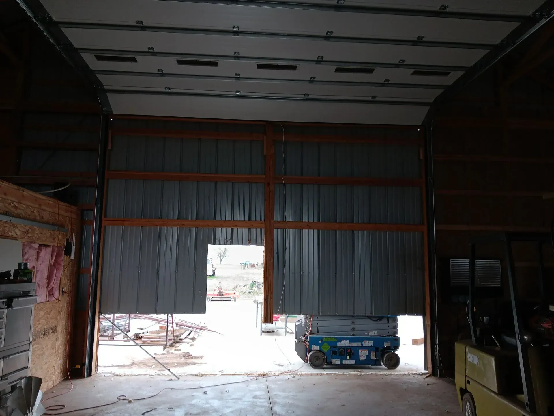 A large garage door is open and a blue scissor lift is parked in the garage.
