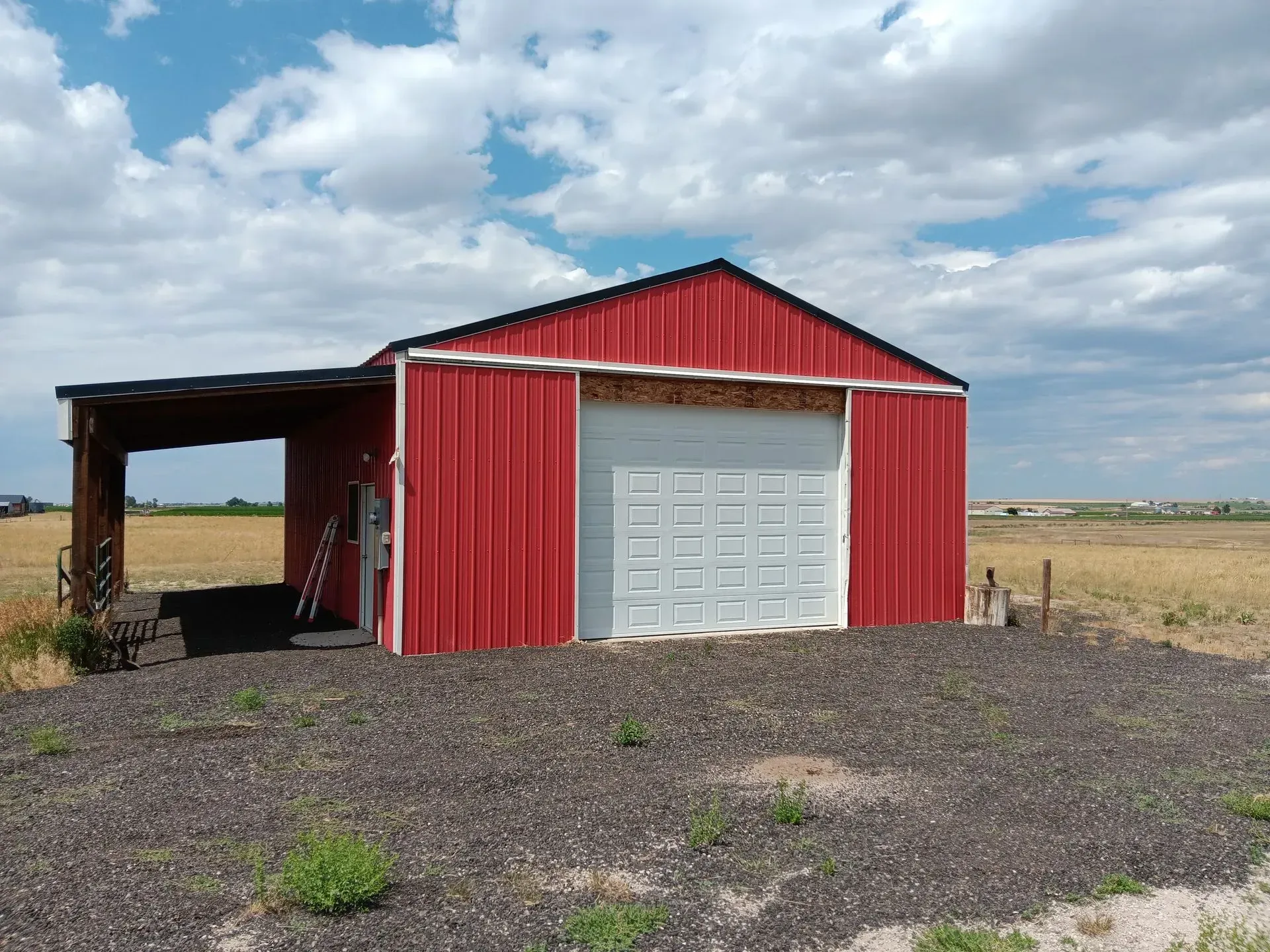 A red barn with a white garage door is in the middle of a field.