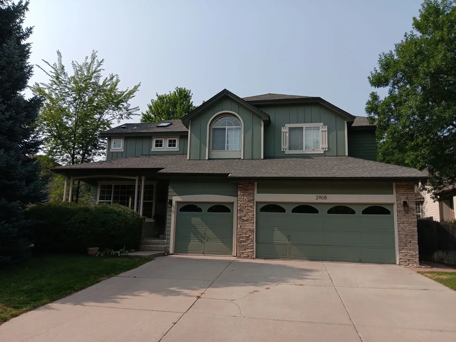 A green house with two garage doors and a driveway