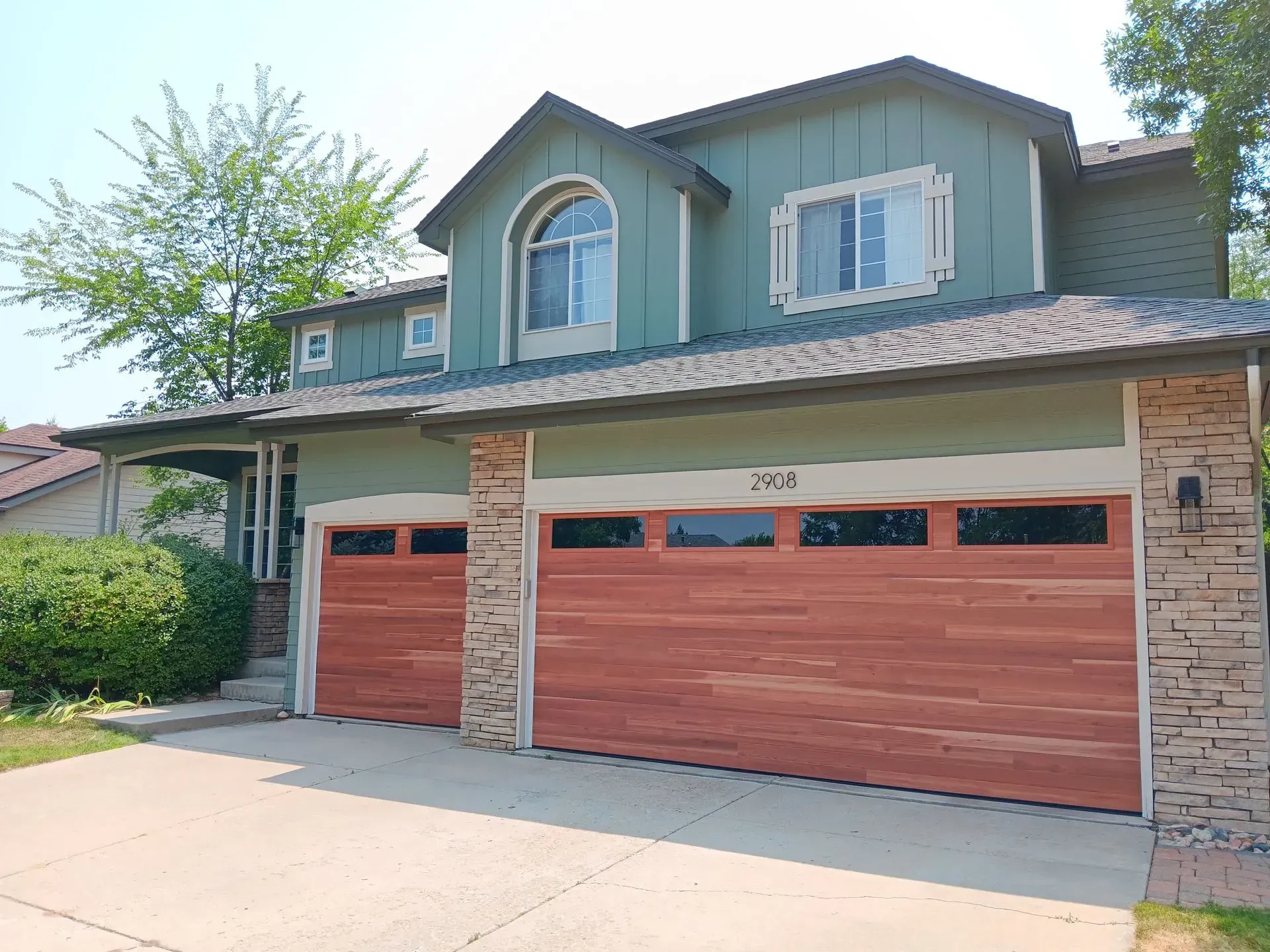 A large house with a green siding and a brown garage door.