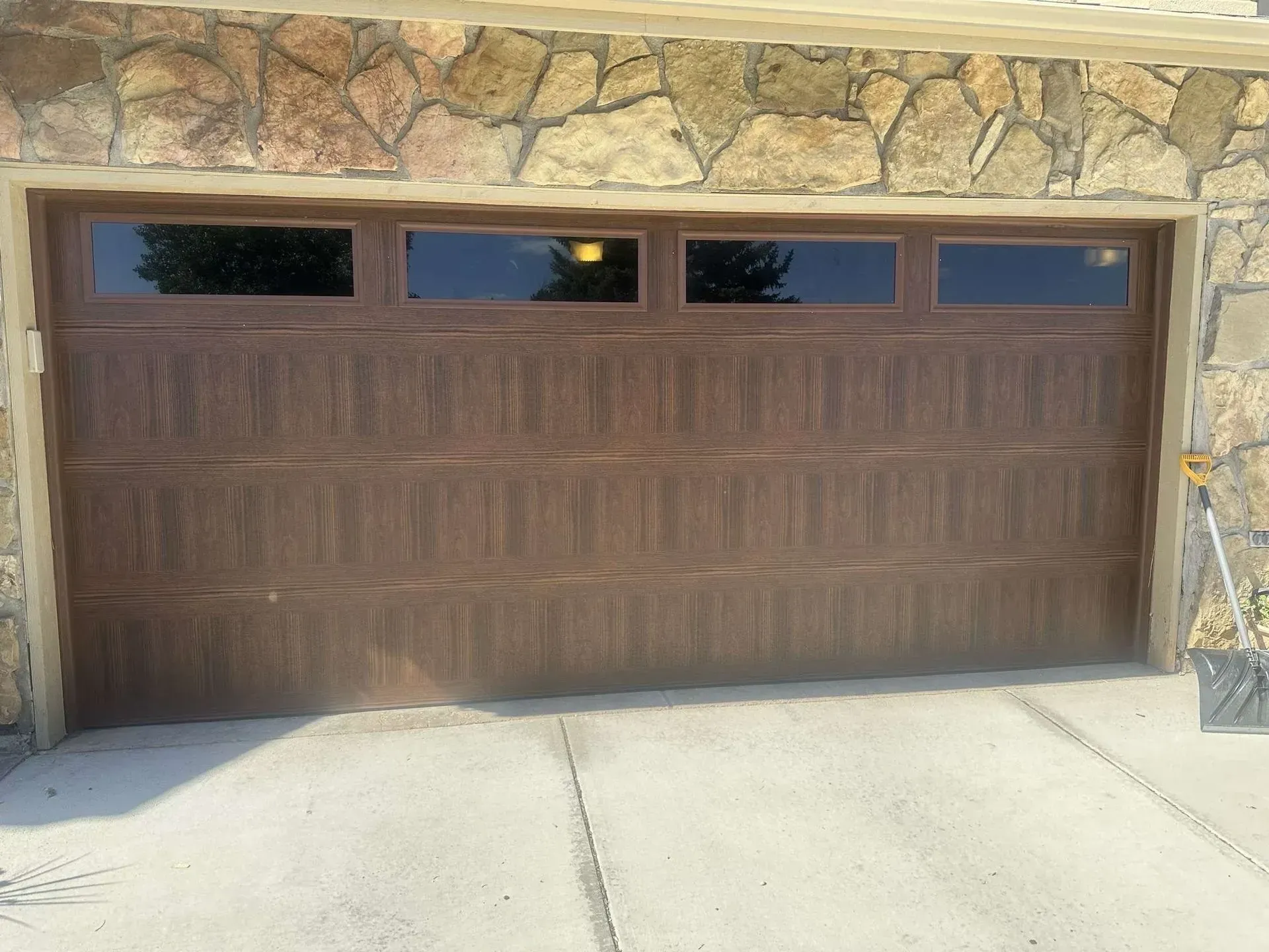 A brown garage door is sitting in front of a stone wall.