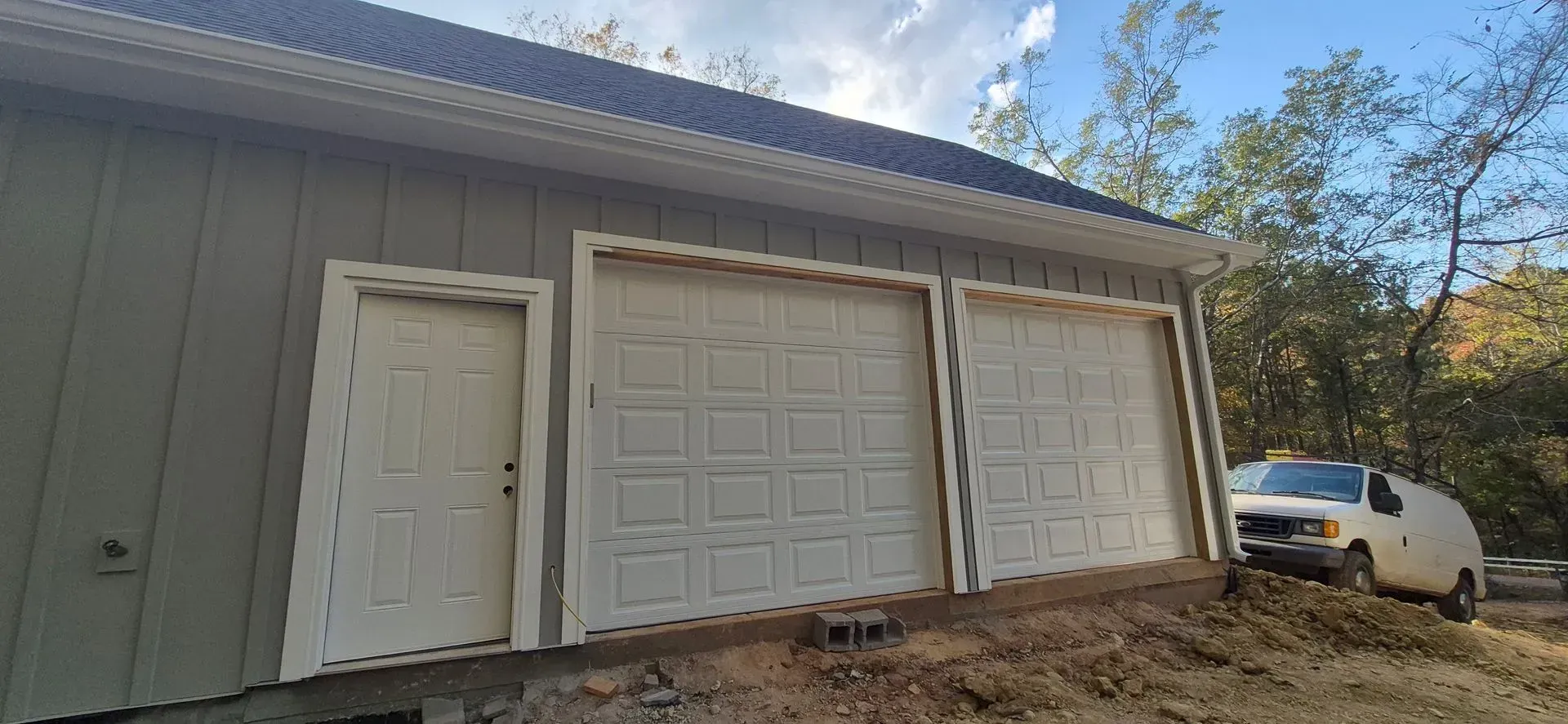 A white van is parked in front of a garage with three garage doors.
