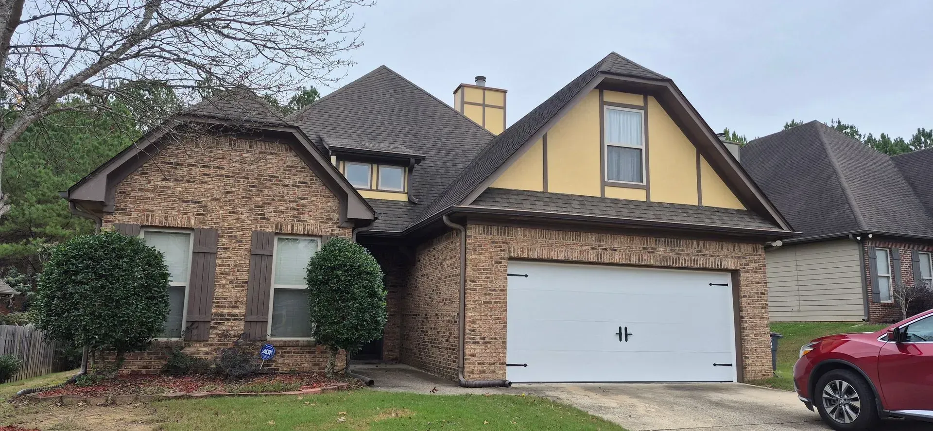 A red car is parked in front of a large brick house.
