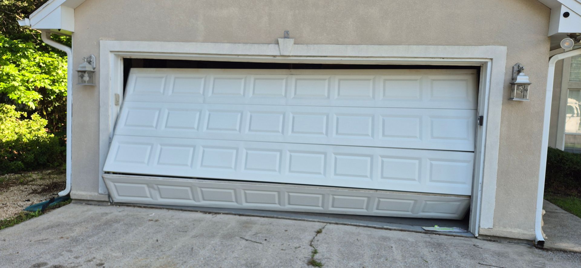 A white car is parked in front of a house with two garage doors.