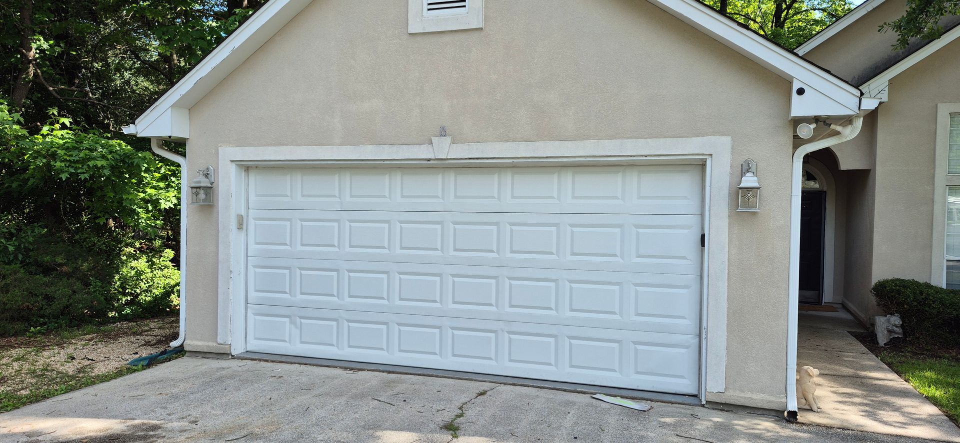 A white car is parked in front of a house that has a green siding