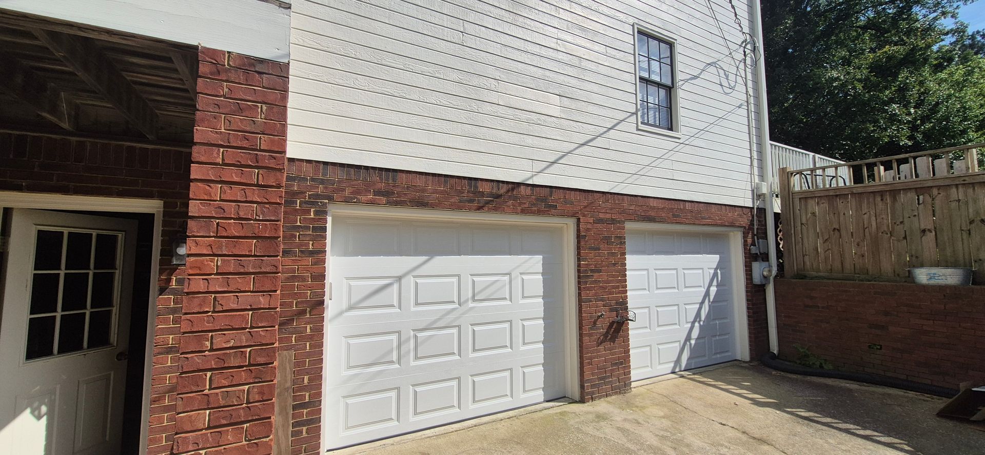 A two-story building with two garage doors. The bottom level is brick, and the top level is white siding.
