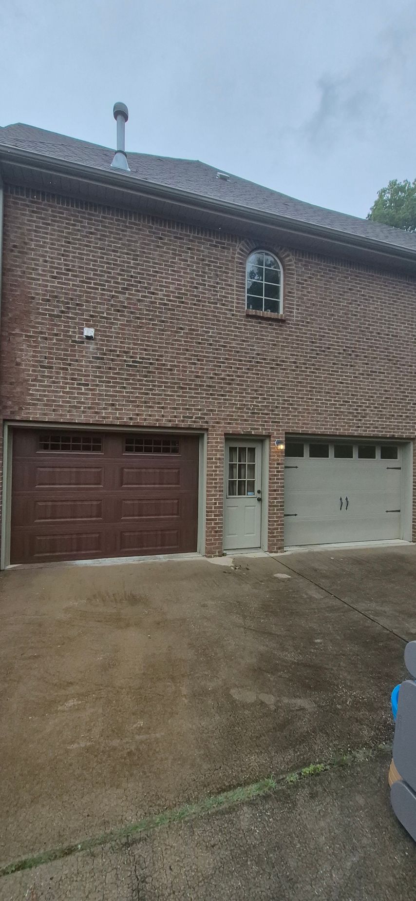 A brick building with a brown garage door on the left and a gray garage door on the right, with a small door in between.
