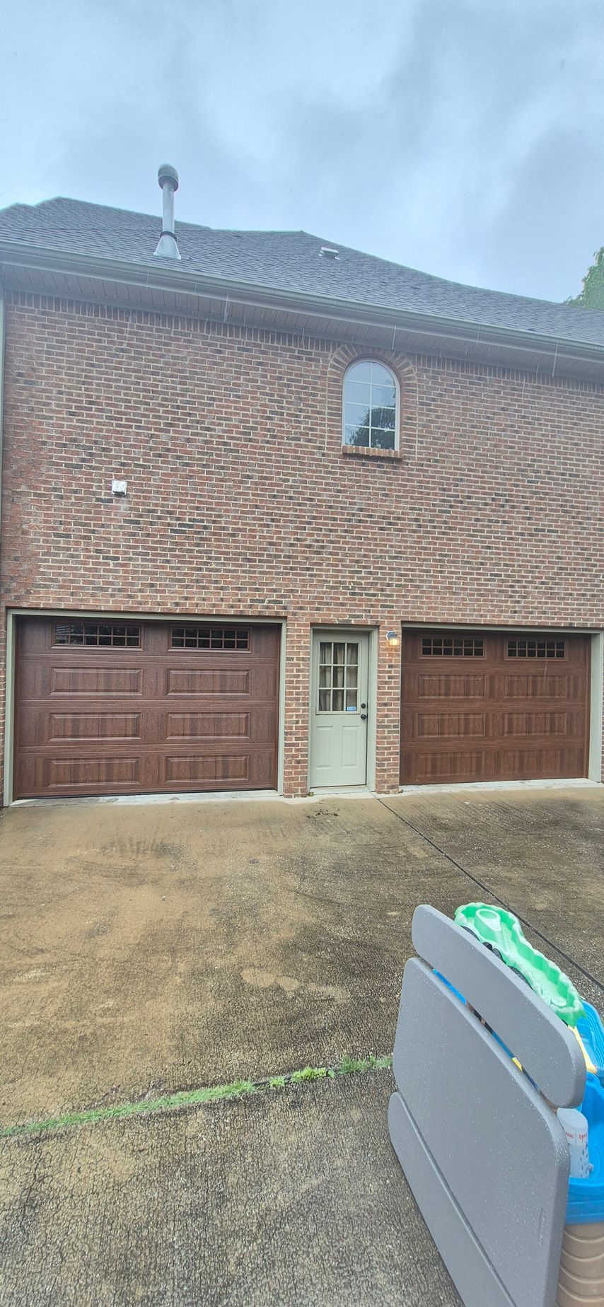 Brick building with two garage doors, a small door, and an arched window. Brown garage doors and tan door, against a brick wall.