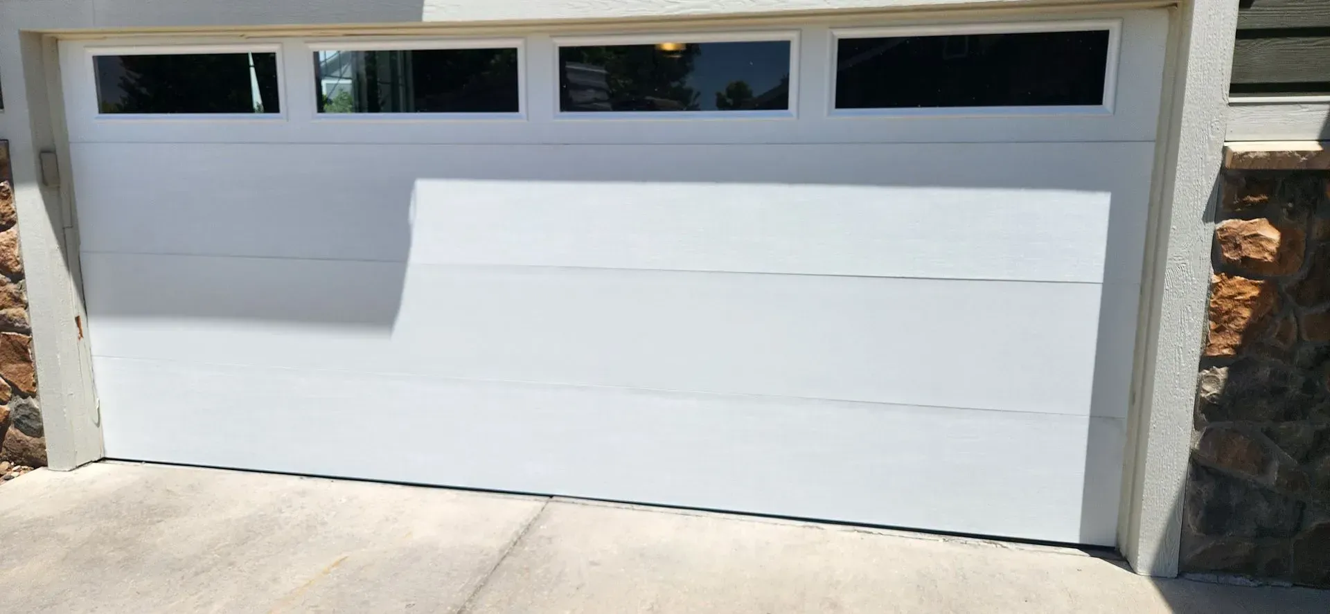 A white garage door is sitting on a concrete driveway next to a stone wall.