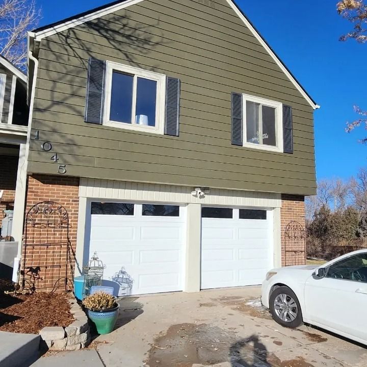 A white car is parked in front of a house that has a green siding