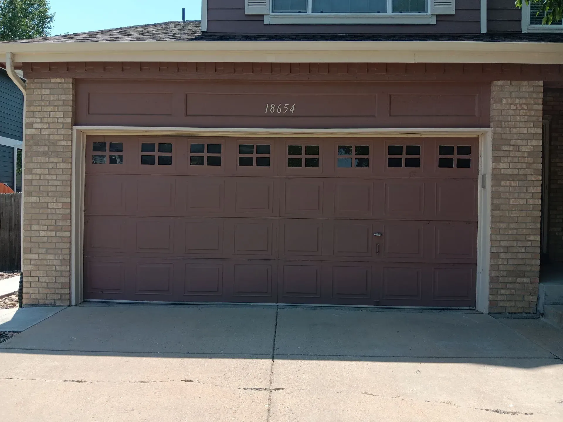 A brown garage door is sitting in front of a brick house.