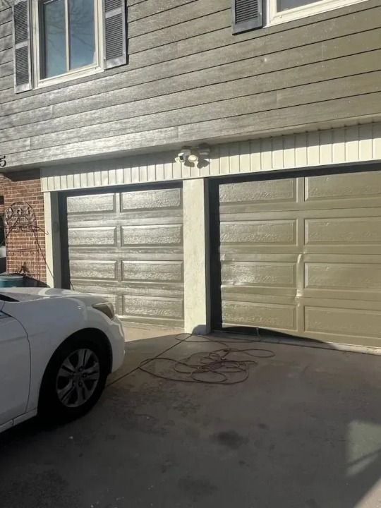 A white car is parked in front of a house with two garage doors.