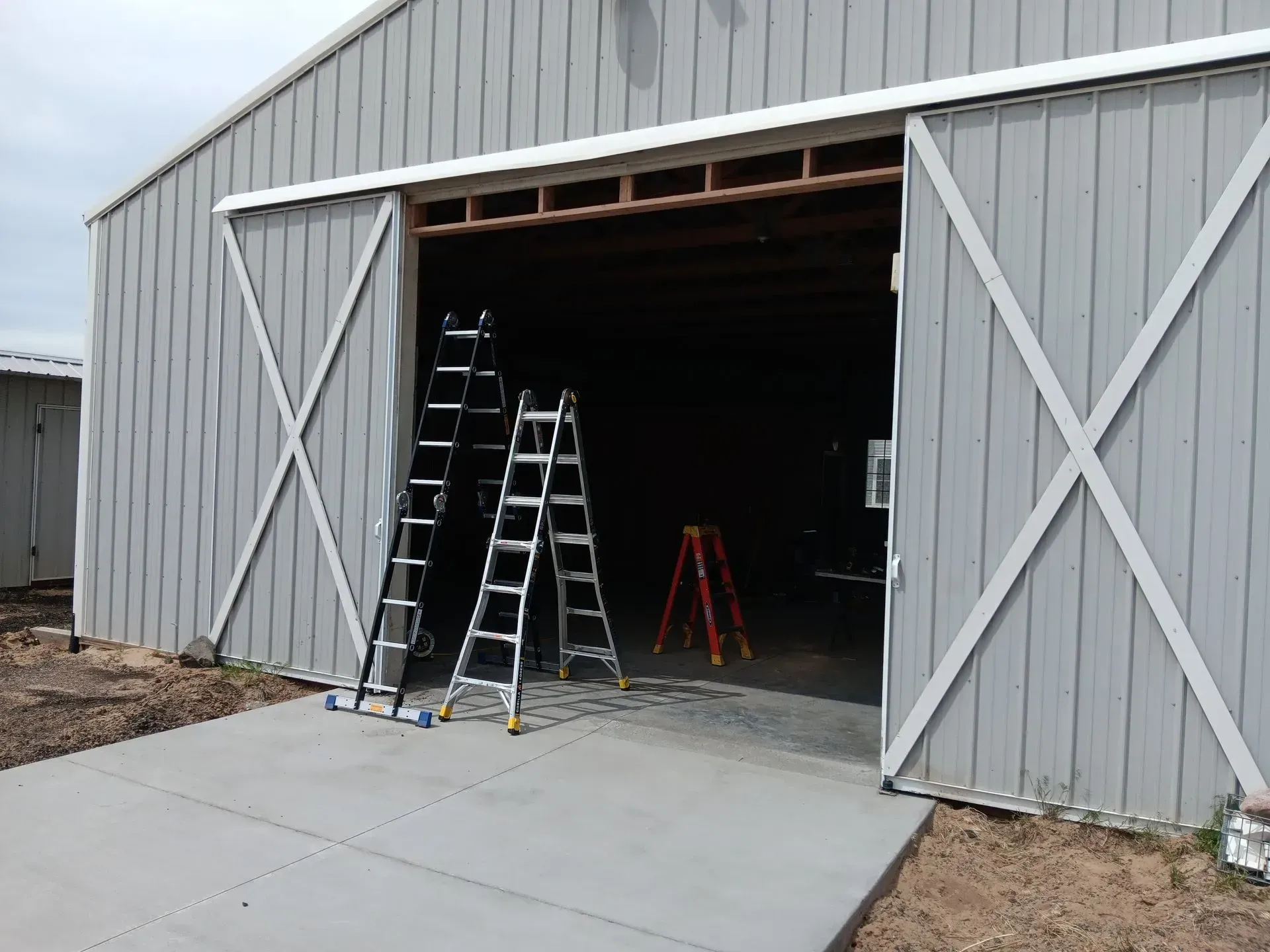 A gray barn with a sliding barn door and ladders in front of it.