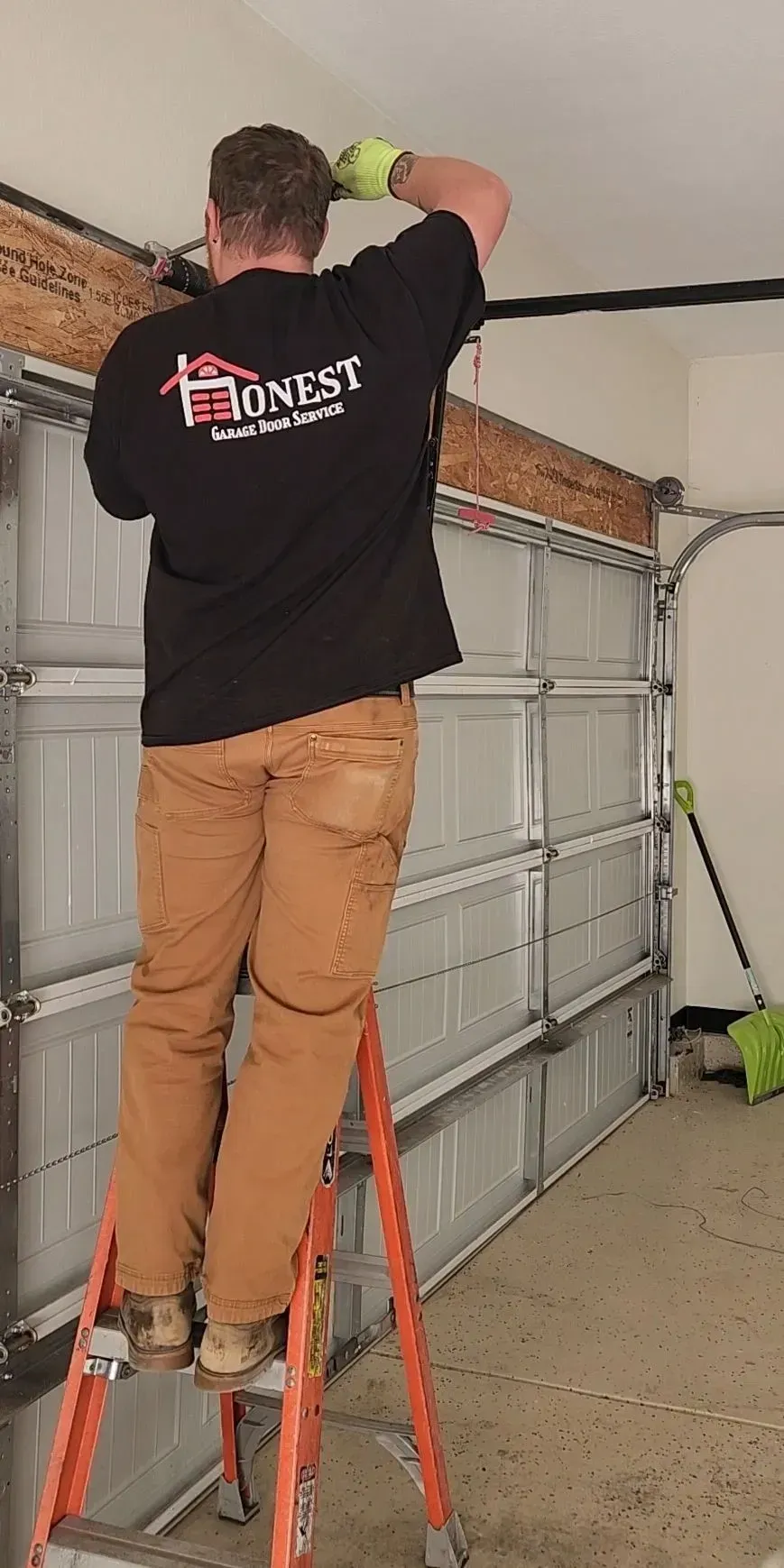 A man is standing on a ladder fixing a garage door.