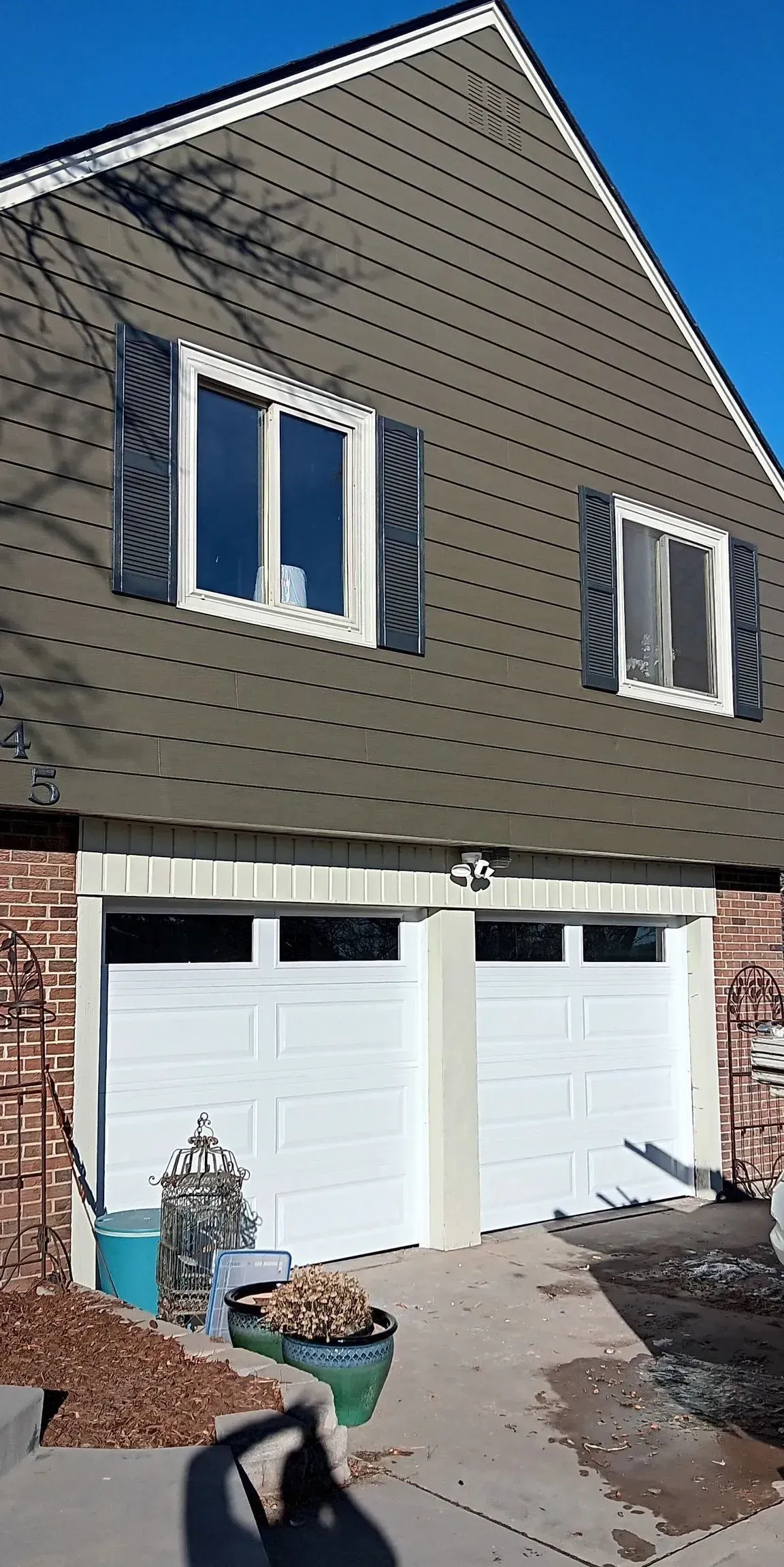 A house with two garage doors and two windows on a sunny day.