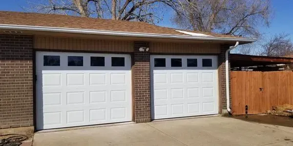 A house with two white garage doors and a wooden fence.