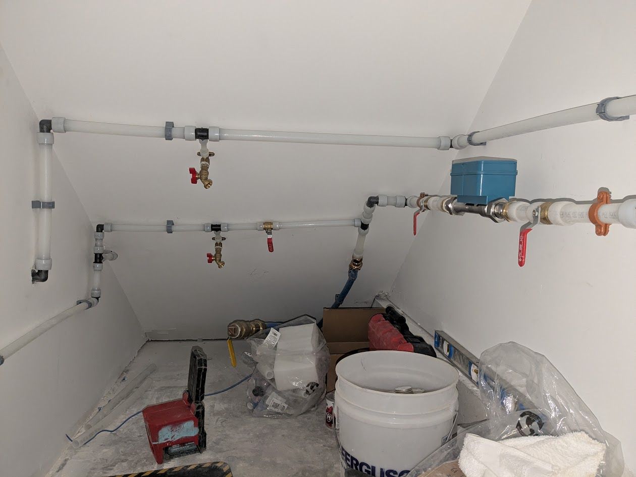 Small attic room with exposed pipes, valves, buckets, and construction materials on the floor.