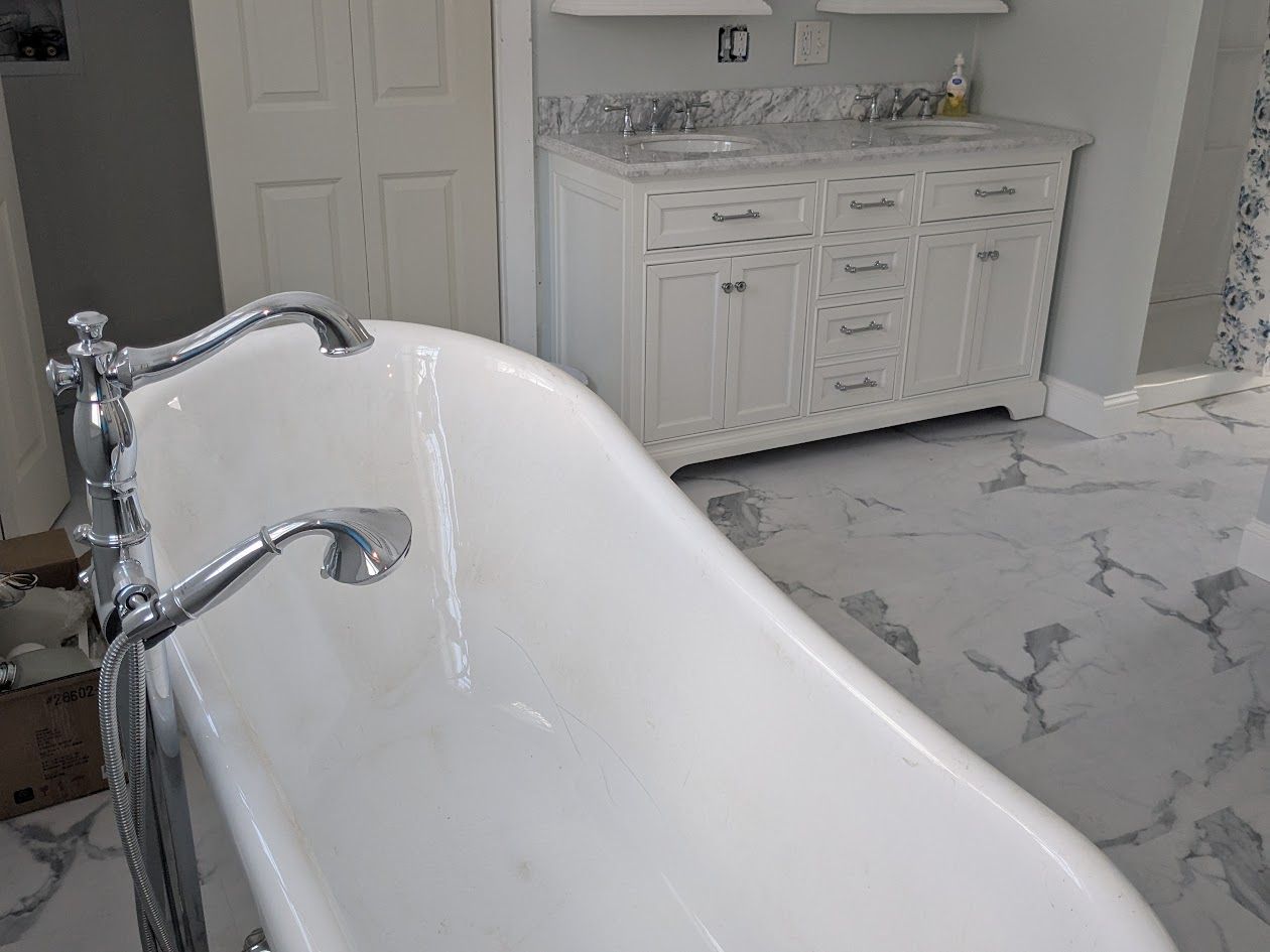 White bathroom with clawfoot tub, chrome faucets, and marble floor facing a double vanity.