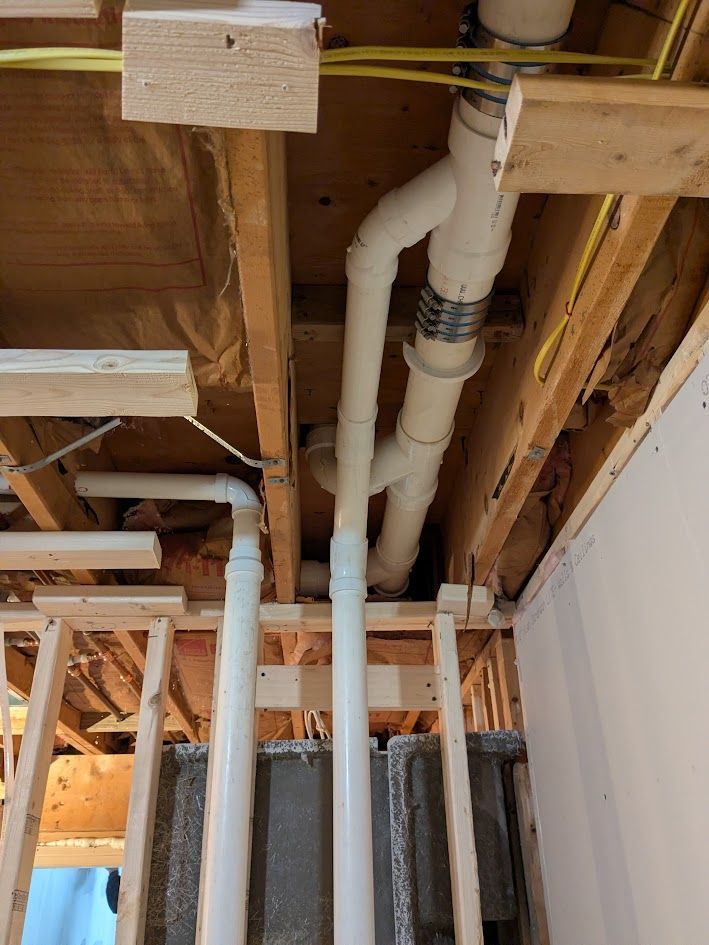 Exposed ceiling pipes and wiring in an unfinished room with wooden framing and insulation