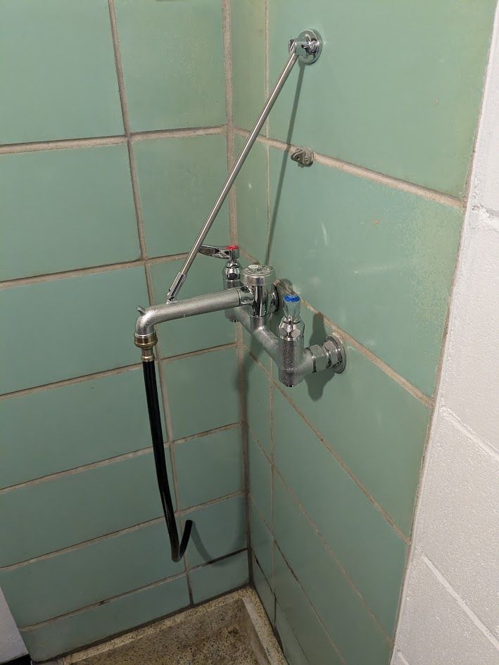 Wall-mounted shower mixer with handheld hose in a mint-green tiled bathroom corner