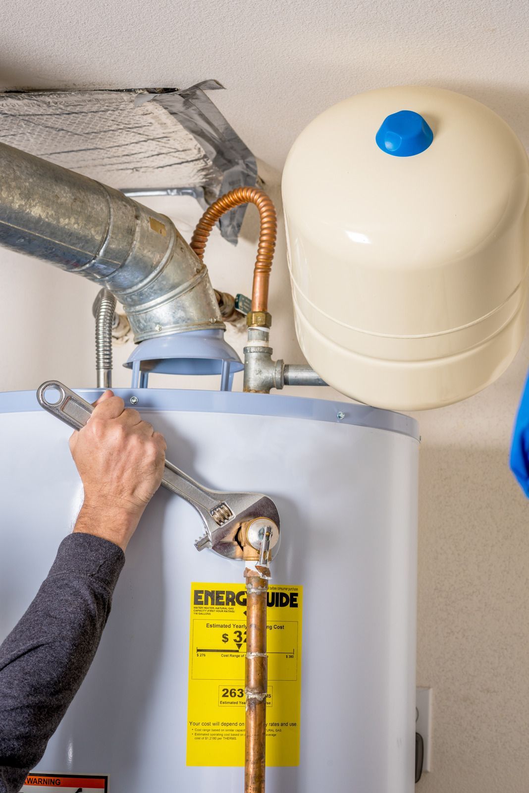 Hands inspecting a water heater with pipes and expansion tank in a utility room