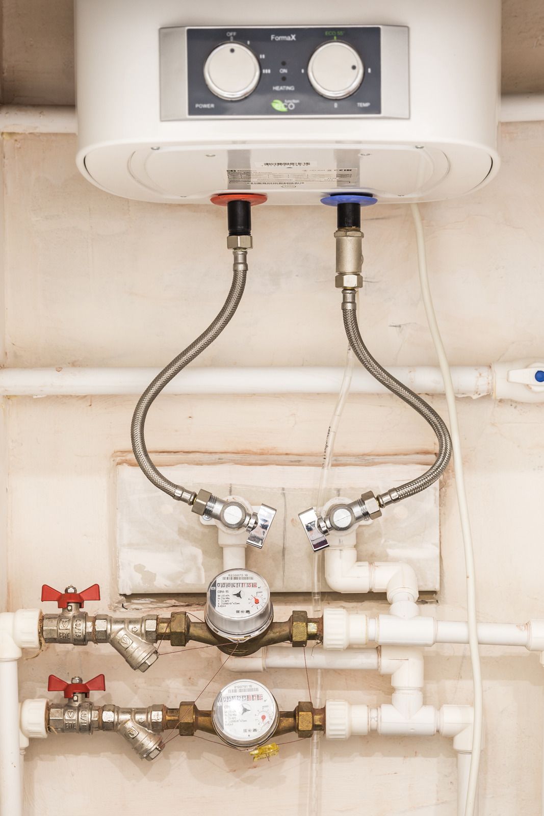 Wall-mounted water heater with pipes, valves, and flexible hoses in a utility room.