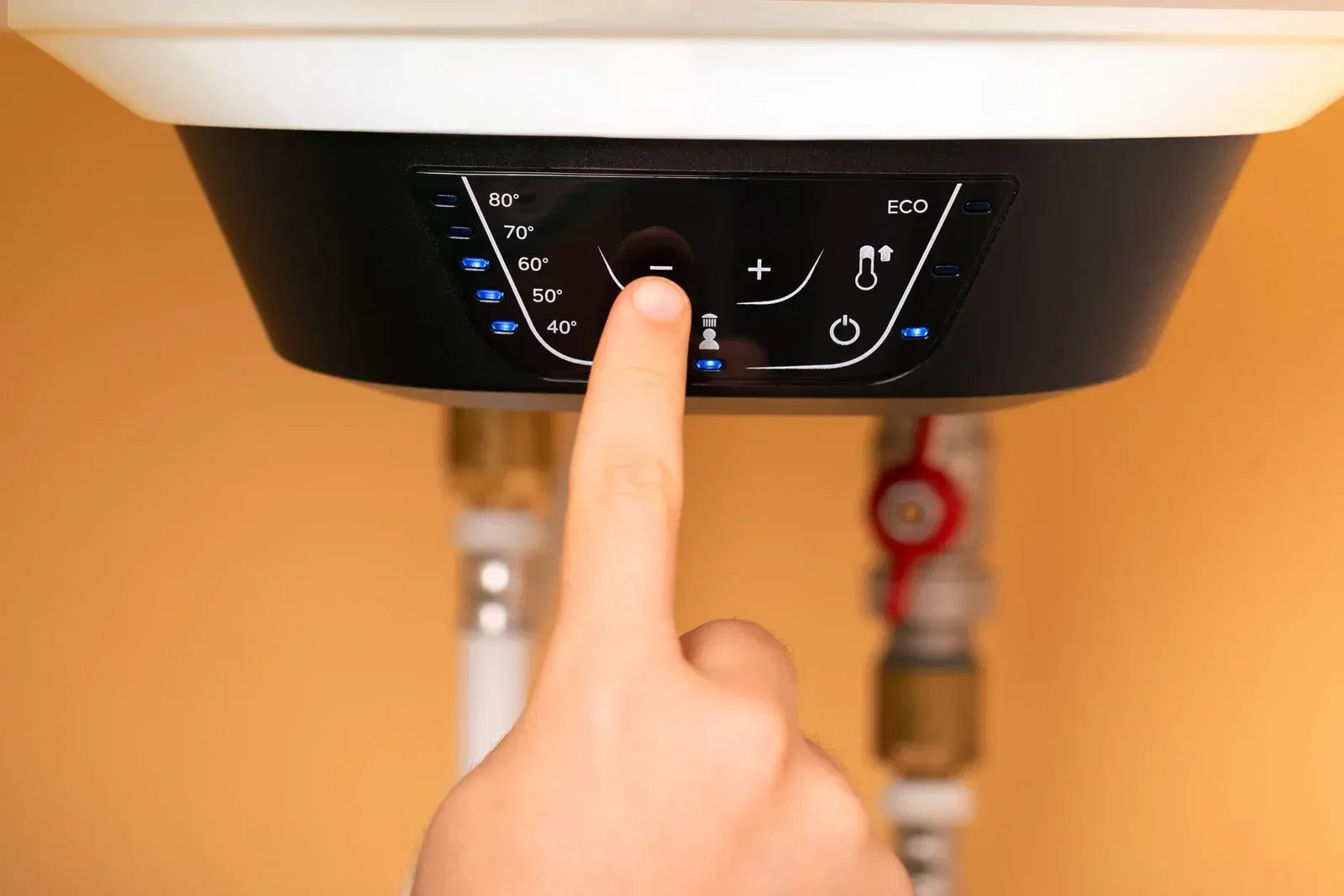 Hand pressing control panel on a wall-mounted boiler with temperature display and buttons