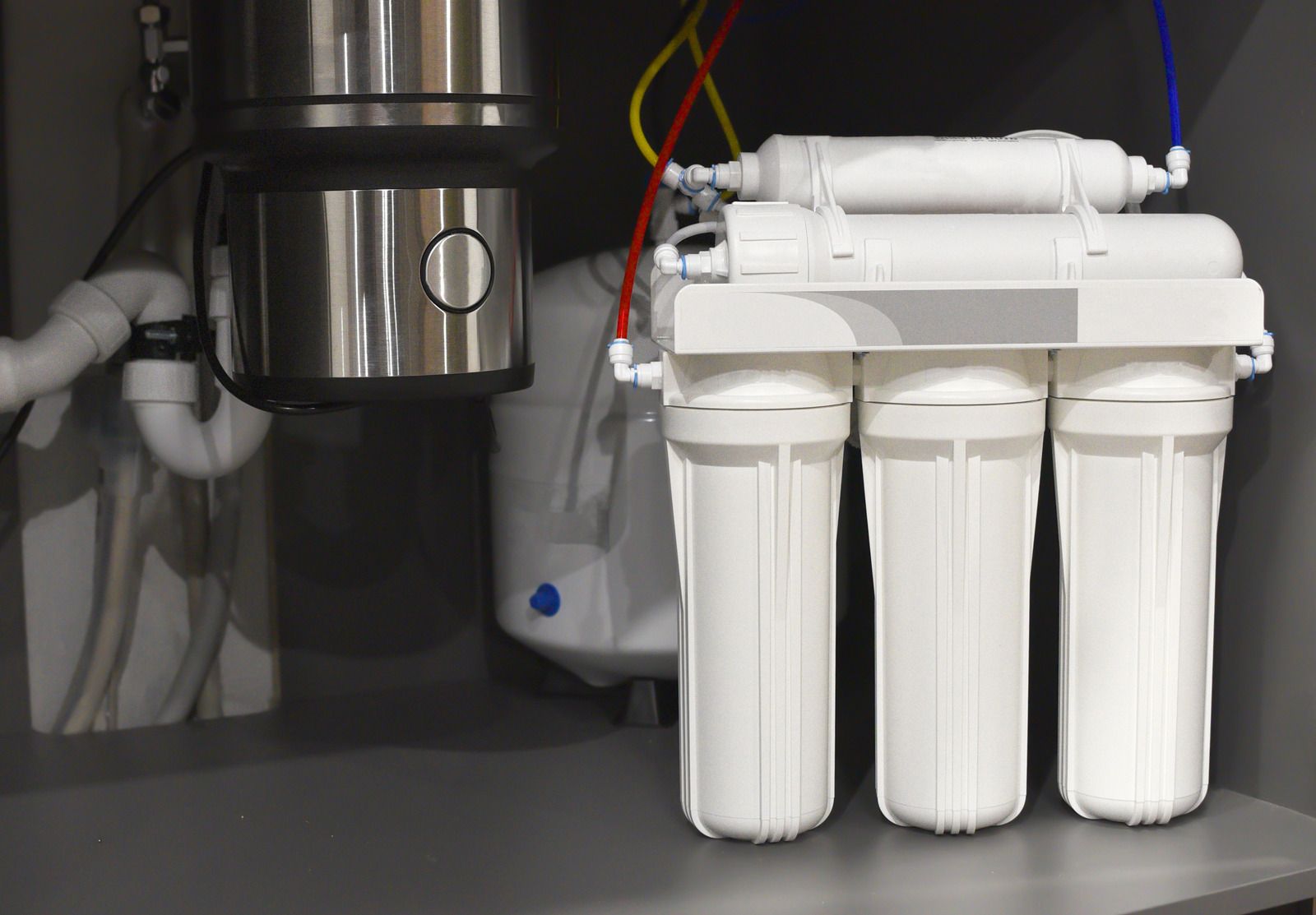 Under-sink water filter system with three white cartridge filters and connected tubing on a shelf