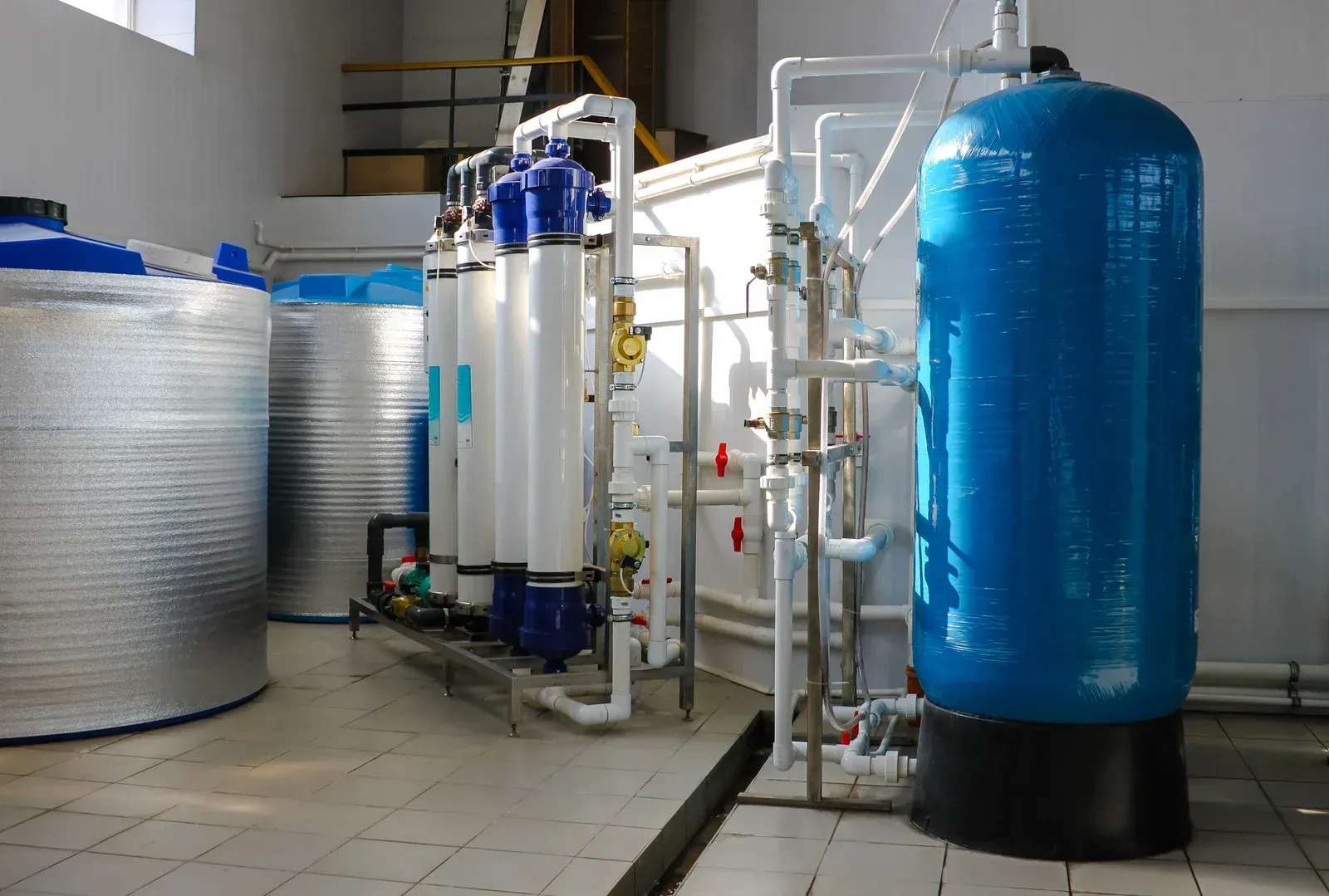 Industrial water filtration tanks and pipes in a utility room, including a large blue pressure tank.